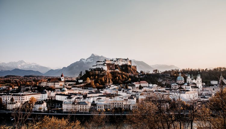 Ansicht von Salzburg, Österreich, mit der Festung Hohensalzburg auf einem Hügel und Bergen im Hintergrund bei Sonnenuntergang.