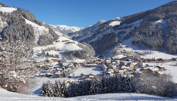 Ein verschneites Bergdorf mit Häusern inmitten von Kiefern unter einem strahlend blauen Himmel.