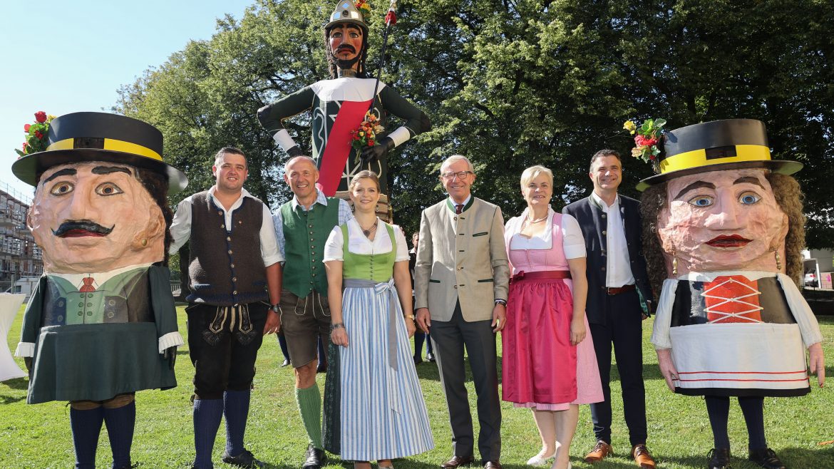 Acht Personen in traditioneller österreichischer Tracht stehen mit zwei großen Festspielpuppen und einer großen Soldatenfigur im Freien.