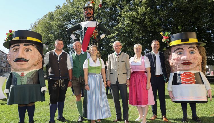 Acht Personen in traditioneller österreichischer Tracht stehen mit zwei großen Festspielpuppen und einer großen Soldatenfigur im Freien.