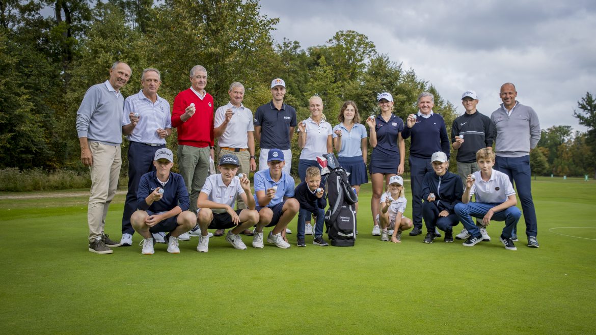 Eine Gruppe von Personen, darunter Kinder und Erwachsene, posieren gemeinsam auf einem Golfplatz und halten Trophäen.
