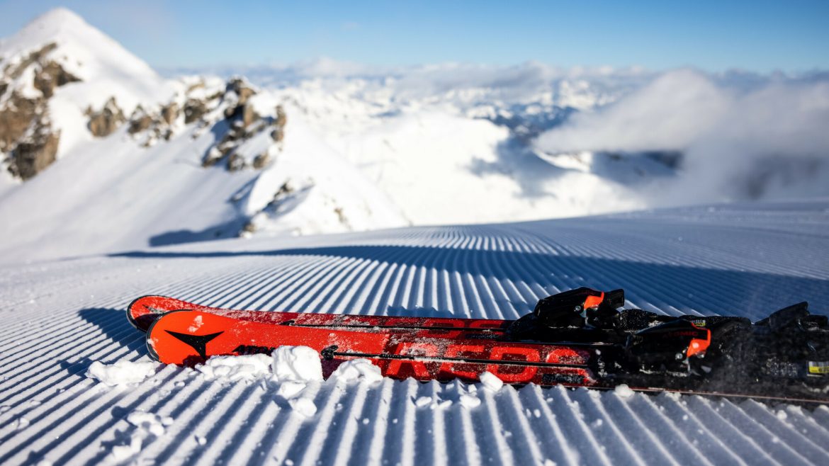 Ein Paar rote Skier, die auf frisch präpariertem Schnee ruhen, mit verschneiten Bergen im Hintergrund.