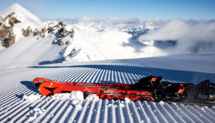 Ein Paar rote Skier, die auf frisch präpariertem Schnee ruhen, mit verschneiten Bergen im Hintergrund.