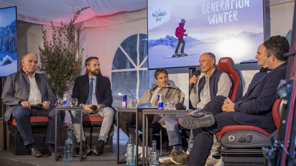 Sechs Männer sitzen auf der Bühne und führen eine Podiumsdiskussion vor zwei Bildschirmen, auf denen "Generation Winter" zu lesen ist.