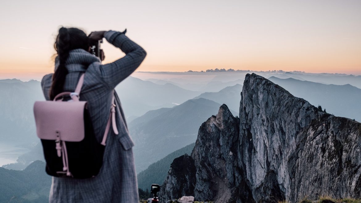Person mit Rucksack, die ein Foto von zerklüfteten Berggipfeln bei Sonnenaufgang oder Sonnenuntergang macht.