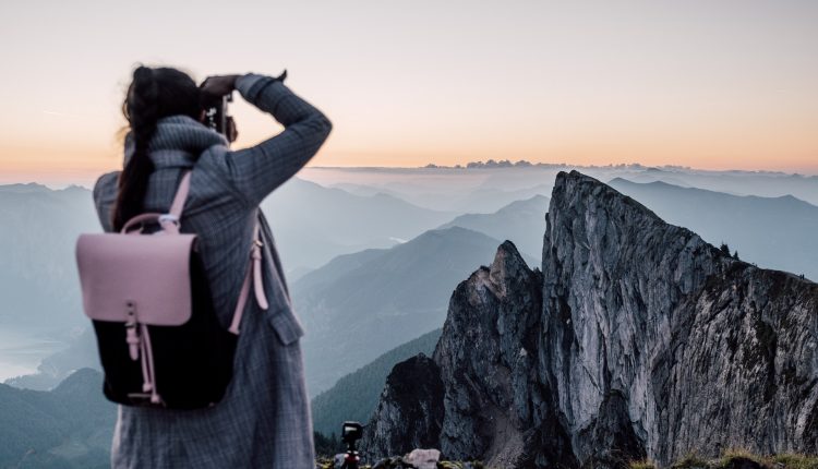 Person mit Rucksack, die ein Foto von zerklüfteten Berggipfeln bei Sonnenaufgang oder Sonnenuntergang macht.
