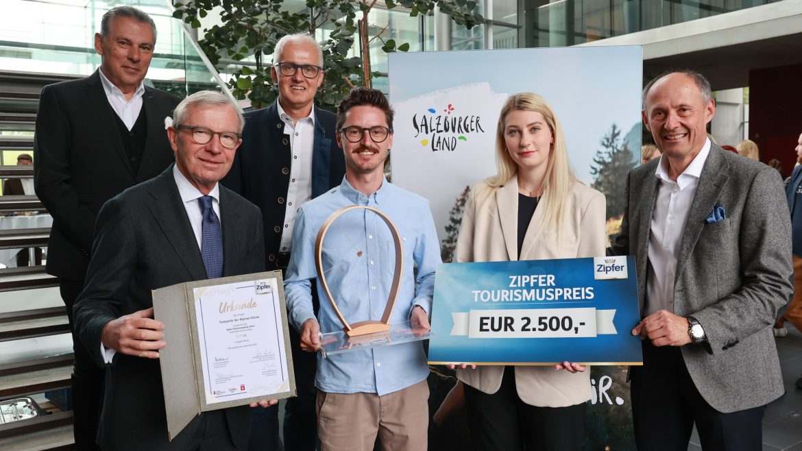 Sechs Personen posieren mit einer Urkunde, einer Trophäe und einem großen Scheck über 2 500 € für den Tourismuspreis in der Halle.
