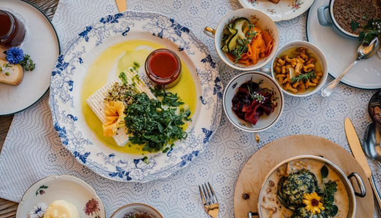 Ein Tisch mit verschiedenen bunten Gerichten, darunter Salate, Grünzeug, Soßen und Brot auf eleganten Tellern.
