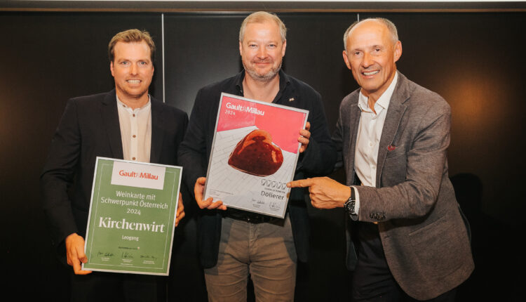 Drei Männer stehen lächelnd da, halten und zeigen auf die Gault&Millau 2024 Restaurant- und Kuchenpreise.