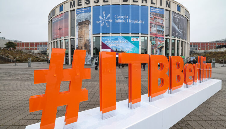 Großes orangefarbenes #ITBBerlin-Schild vor dem Gebäude der Messe Berlin mit darüber angebrachten Veranstaltungsbannern.