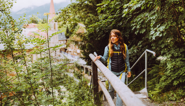 Frau geht einen Waldweg hinauf, im Hintergrund sind ein Dorf und ein Kirchturm zu sehen.