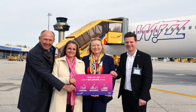 Vier Personen stehen lächelnd vor einem Flugzeug von Wizz Air und halten ein leuchtend rosa Zielschild in der Hand.