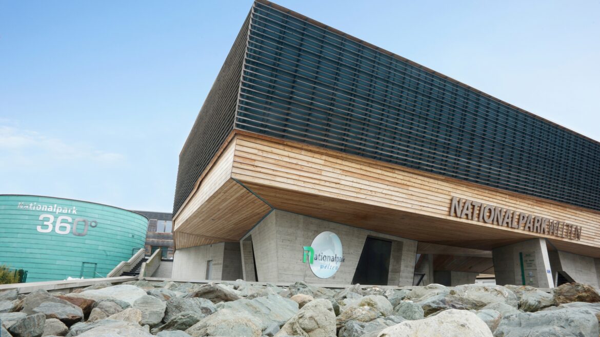 Modernes Gebäude mit Holz- und Glasfassade, Felsen vor dem Gebäude und einem Nationalpark-Schild an der Fassade.