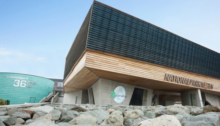 Modernes Gebäude mit Holz- und Glasfassade, Felsen vor dem Gebäude und einem Nationalpark-Schild an der Fassade.