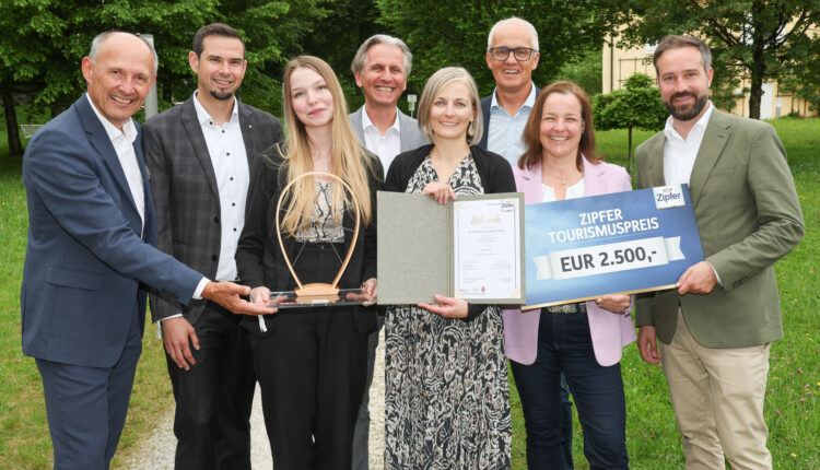 Acht Personen stehen im Freien, lächeln und halten eine Trophäe, eine Urkunde und einen großen Scheck über 2.500 Euro in der Hand.