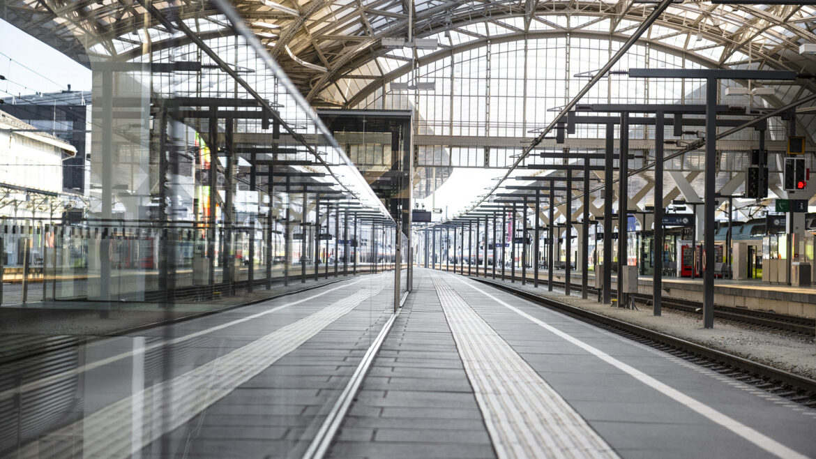 Leeres Bahnhofsgebäude mit Glasdach und Spiegelungen, das mehrere Gleise und Bahnsteige zeigt.