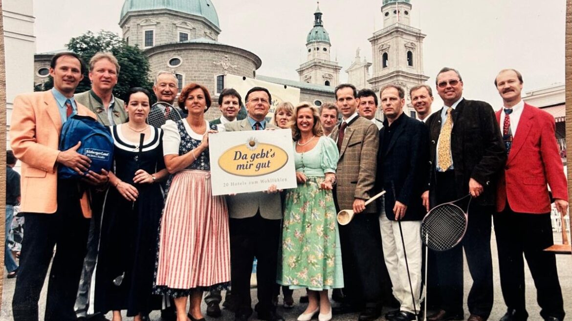 Eine Gruppe von Menschen in historischer Kleidung posiert vor einem historischen Gebäude mit einem Schild und Tennisschlägern.
