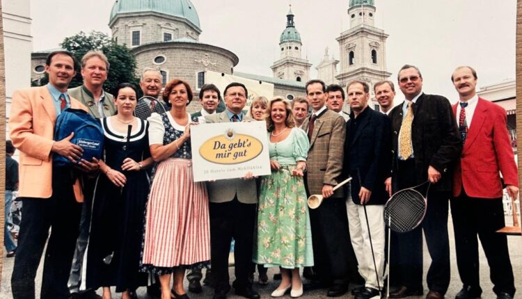 Eine Gruppe von Menschen in historischer Kleidung posiert vor einem historischen Gebäude mit einem Schild und Tennisschlägern.