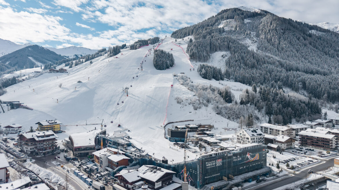 Ein verschneites Skigebiet mit Sesselliften, Pisten und Gebäuden am Fuße eines bewaldeten Berges.