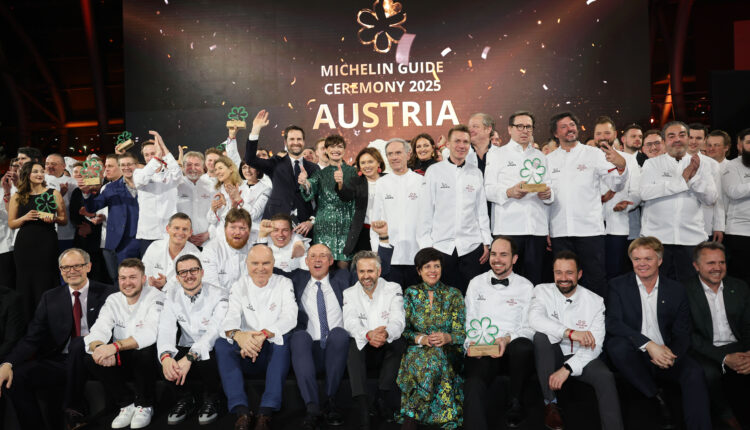 Eine große Gruppe von Köchen in weißen Jacken posiert auf der Bühne bei der Verleihung des Michelin-Führers Österreich 2025.