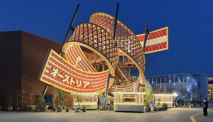 Österreich-Pavillon mit wirbelndem, rot-weiß beleuchtetem Design bei Nacht, gesäumt von Pflanzen und Beschilderung.