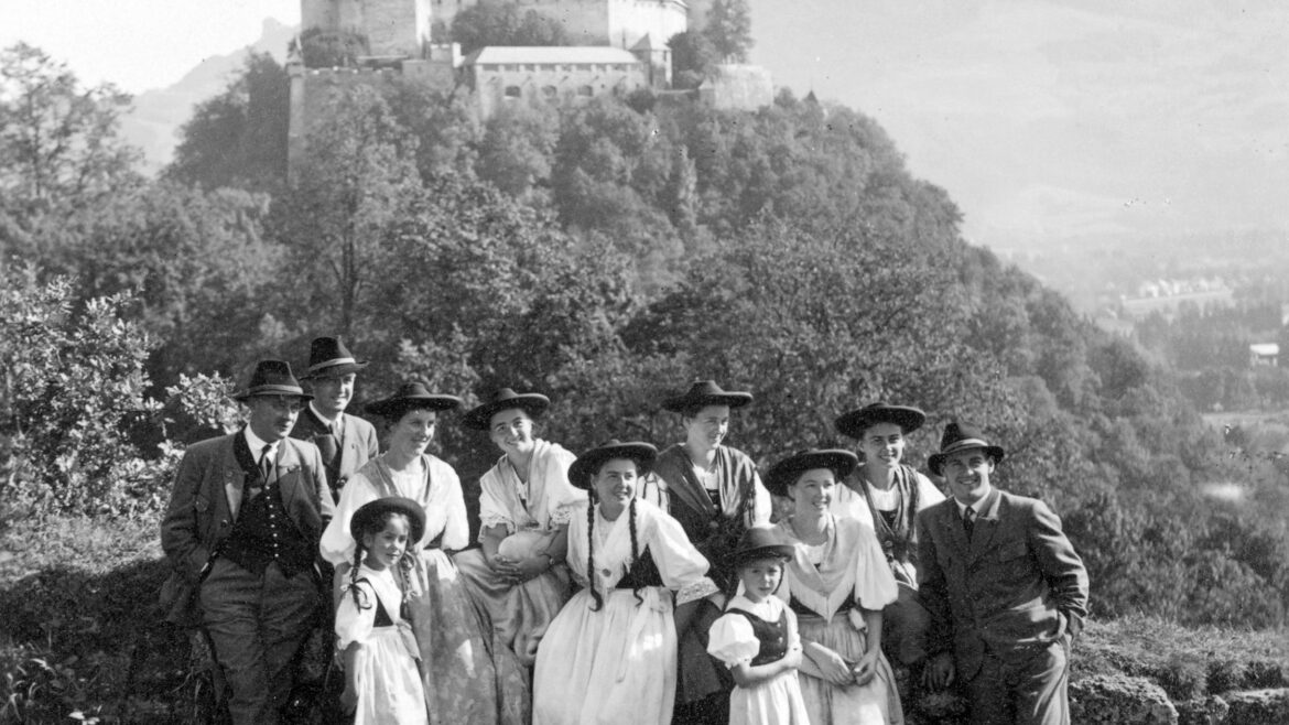 Eine Gruppe in traditioneller Kleidung posiert im Freien mit einer großen Burg auf einem Hügel im Hintergrund.