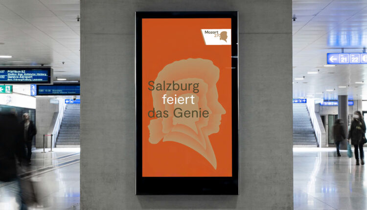 Digitales Plakat in einem Bahnhof mit Mozarts Silhouette und Text: Salzburg feiert das Genie auf orangem Hintergrund.