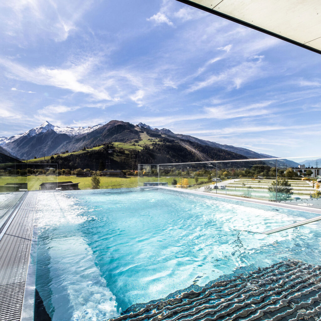 Infinity-Pool mit Bergblick, klarem Himmel und modernem Design unter einem Glasdach.
