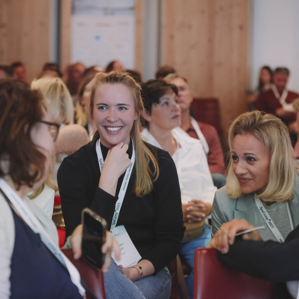 Eine Gruppe von Frauen sitzt bei einer Konferenz oder einem Seminar zusammen, lächelt und unterhält sich.