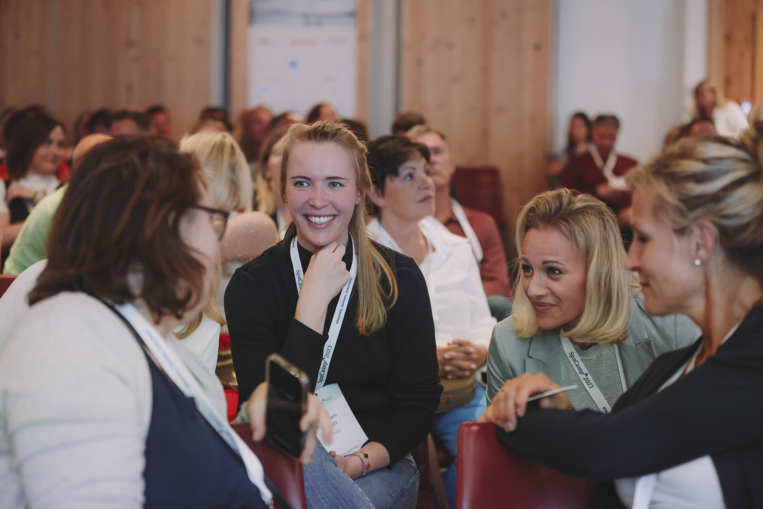 Eine Gruppe von Frauen sitzt bei einer Konferenz oder einem Seminar zusammen, lächelt und unterhält sich.