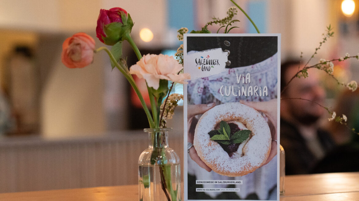 Eine kleine Blumenvase und eine Dessertkarte stehen auf einem Holztisch in einem gemütlichen, gedämpft beleuchteten Restaurant.