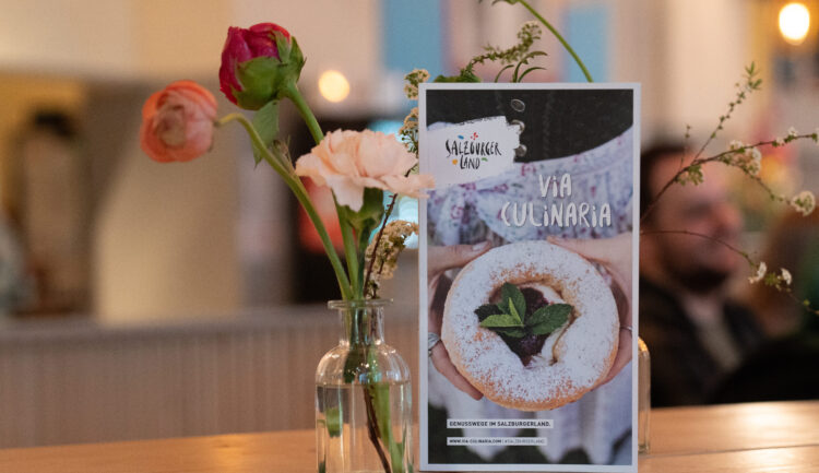 Eine kleine Blumenvase und eine Dessertkarte stehen auf einem Holztisch in einem gemütlichen, gedämpft beleuchteten Restaurant.