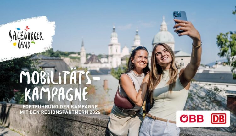 Zwei Frauen lächeln und machen ein Selfie im Freien mit einer Stadtlandschaft und Kuppelgebäuden im Hintergrund.