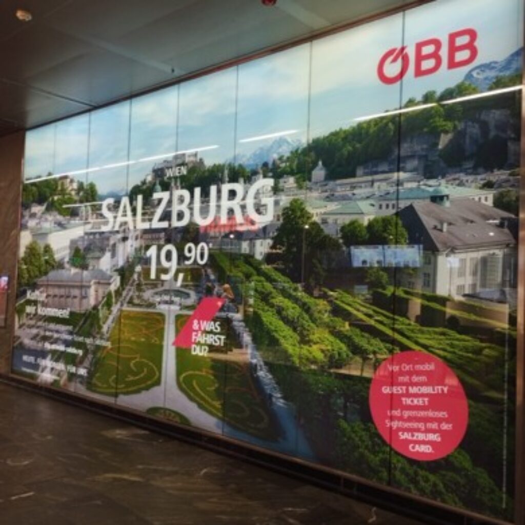 ÖBB-Plakat wirbt für eine Zugfahrt nach Salzburg zum Preis von 19,90 €, mit Stadtansicht und Reiseinformationen.