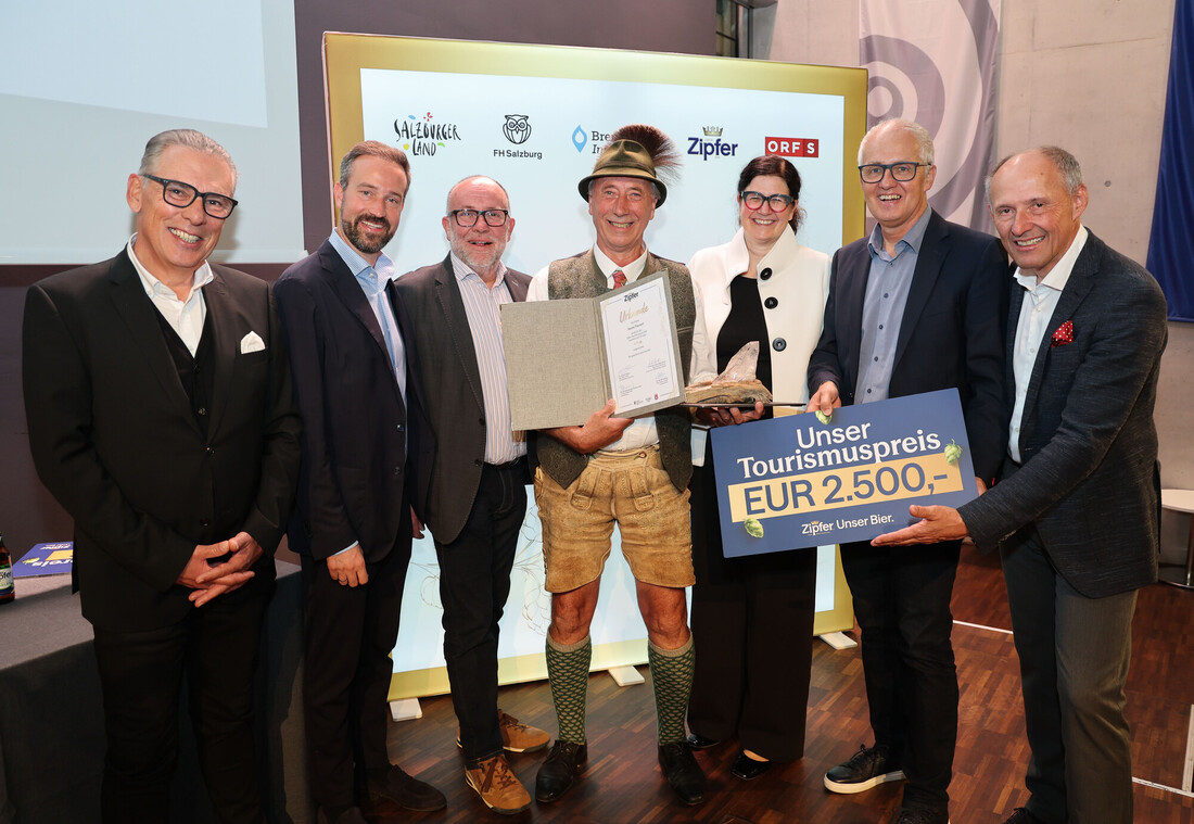 Sieben Personen stehen lächelnd bei einer Preisverleihung, eine hält eine Urkunde in der Hand, eine andere ein Schild mit einem Tourismuspreis von 2 500 €.