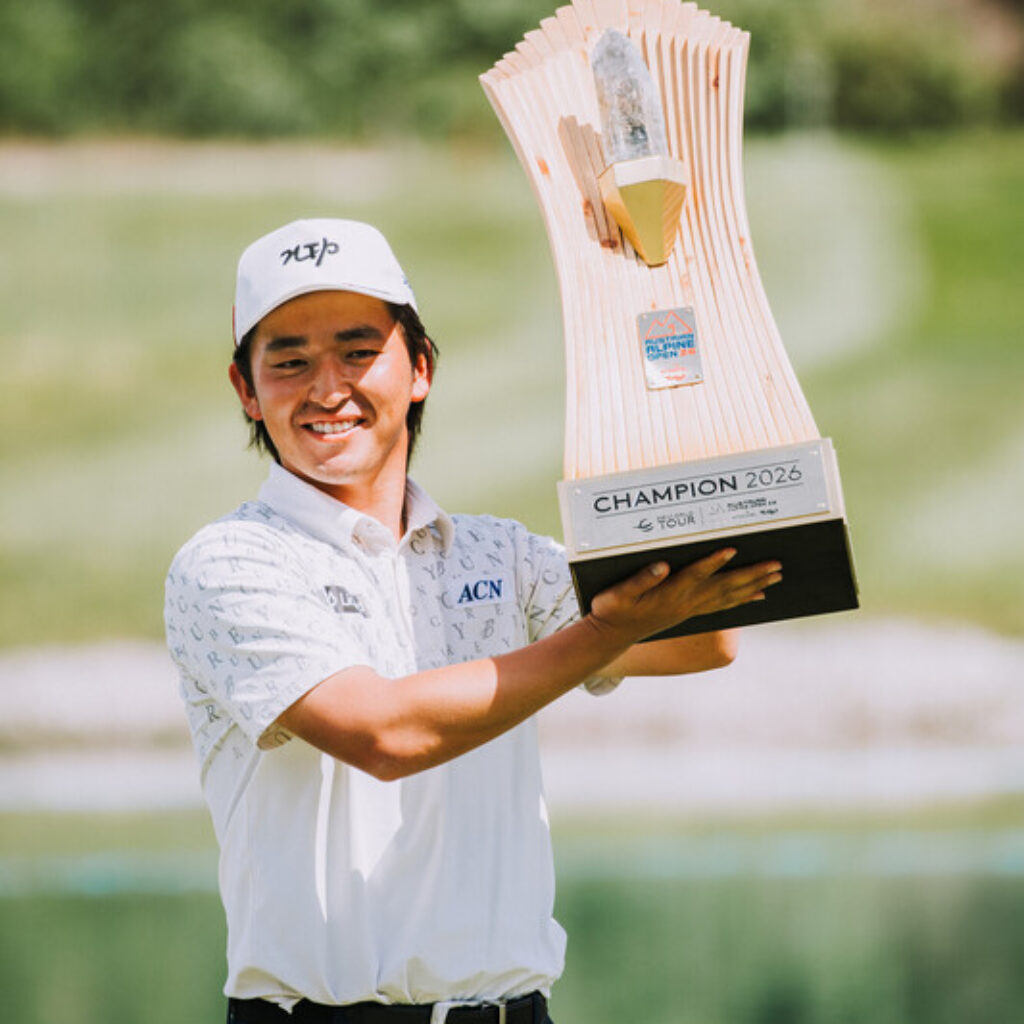 Ein lächelnder Golfer hält eine große Trophäe mit der Aufschrift Champion 2022 auf einem sonnigen Golfplatz hoch.