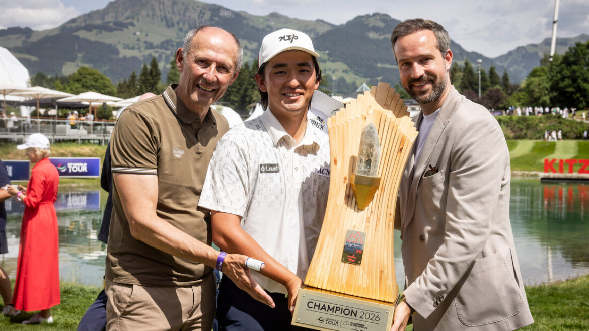Drei lächelnde Männer mit einer großen Golftrophäe im Freien, Berge und See im Hintergrund.