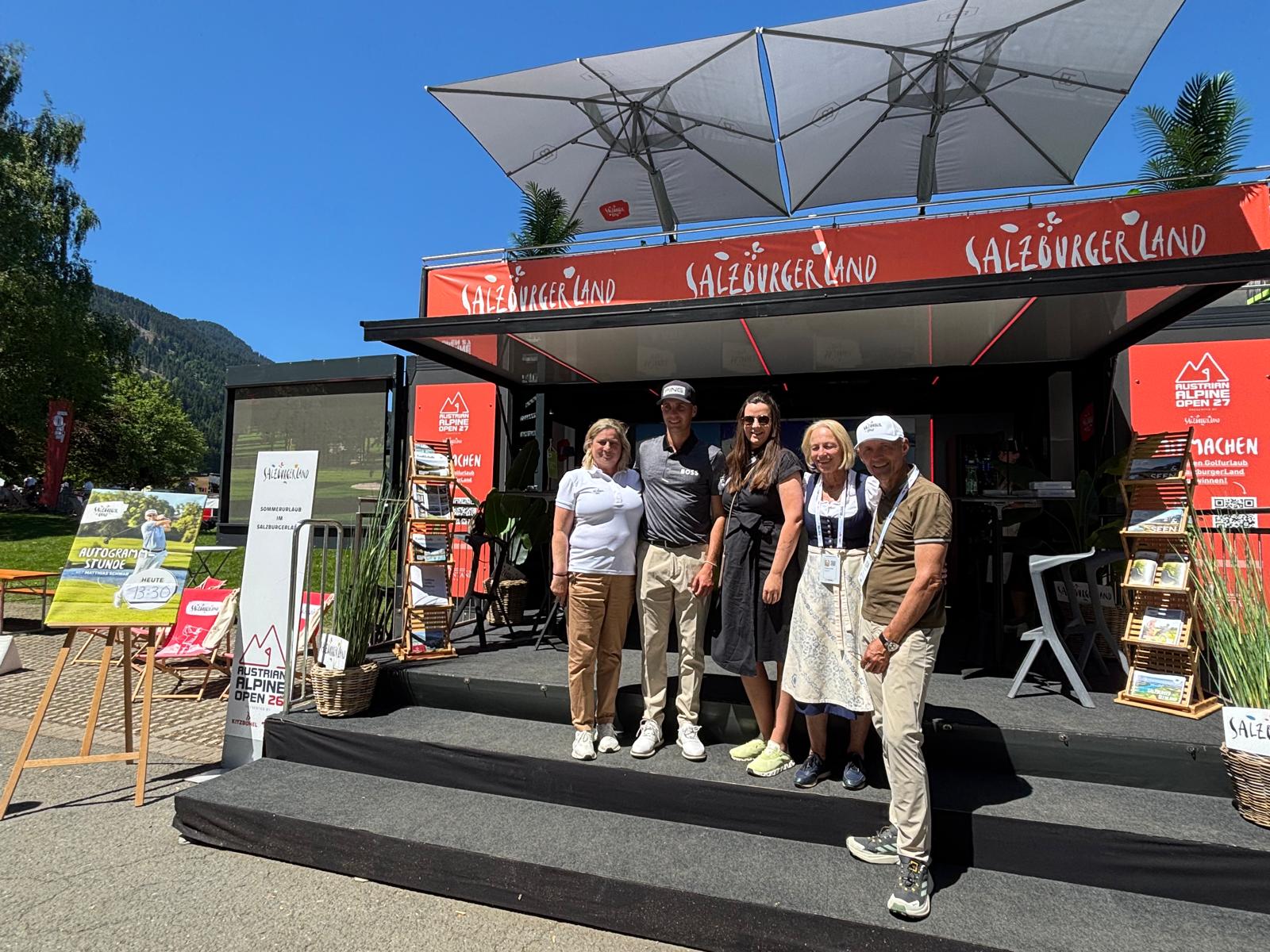 Fünf Personen stehen an einem sonnigen Tag lächelnd vor einem rot-schwarzen SalzburgerLand-Eventstand.