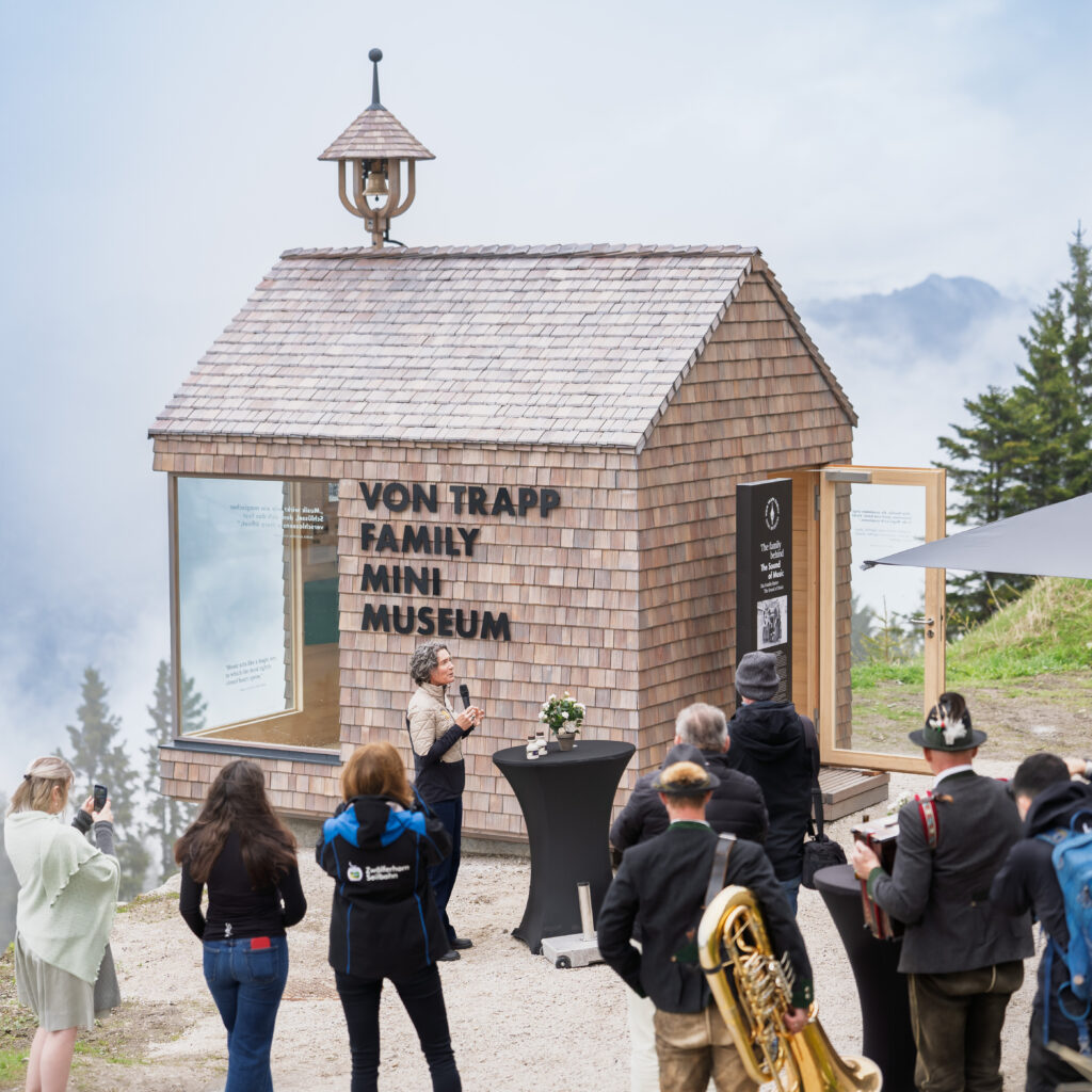 Auf einem Berg steht ein kleines Holzmuseum, vor dem sich eine Menschenmenge versammelt hat; einige machen Fotos.