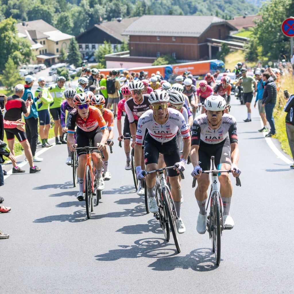 Radfahrer, die auf einer Straße bergauf rasen, umgeben von jubelnden Zuschauern und Fotografen.