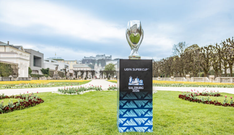 Die Trophäe des UEFA-Supercups auf einem Sockel in einem Garten, auf dem Sockel steht „Salzburg 2026“.