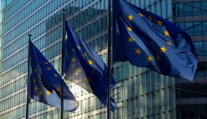 Drei Flaggen der Europäischen Union wehen vor einem modernen Glasgebäude.