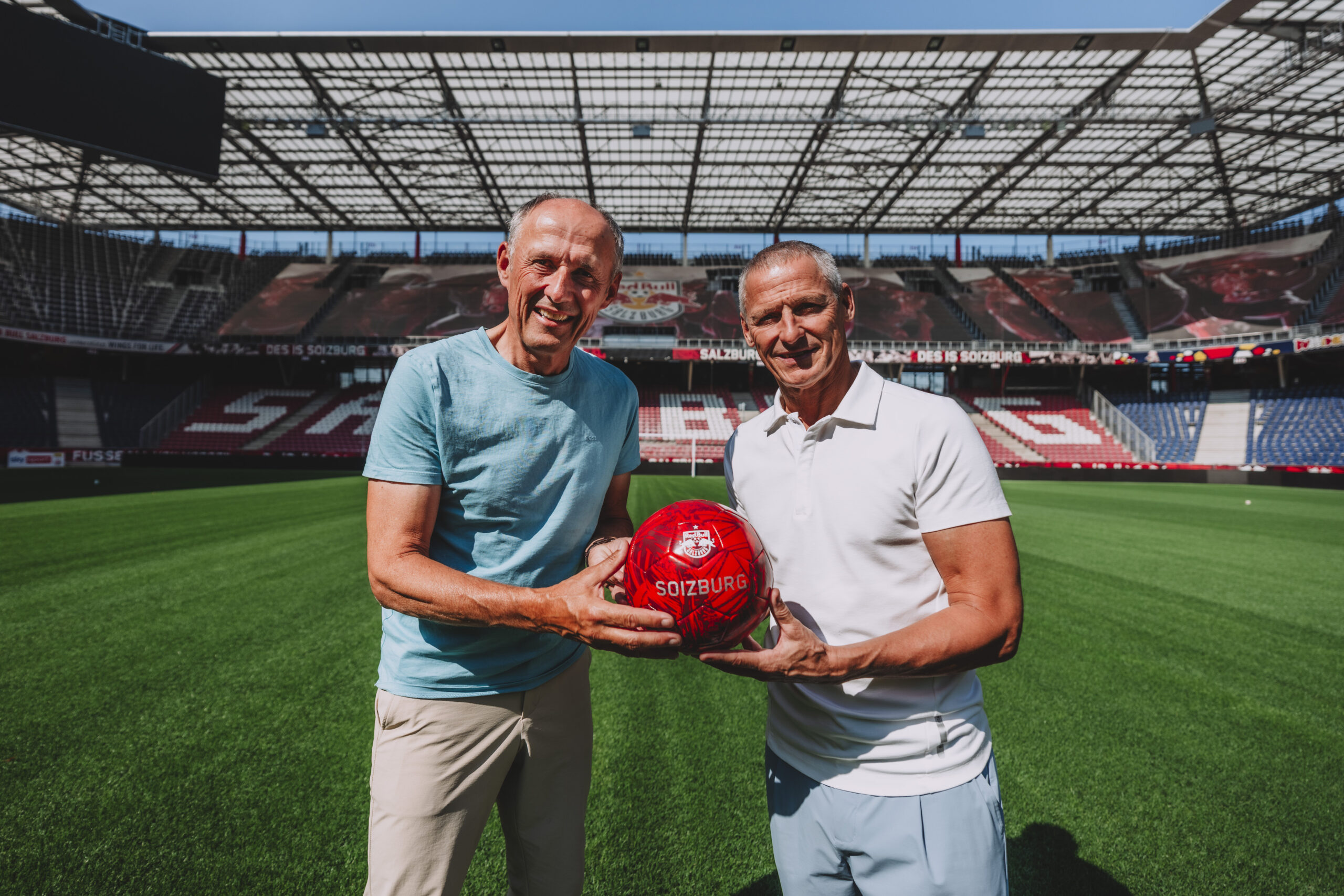 Zwei Männer stehen mit einem roten Ball auf einem Fußballplatz