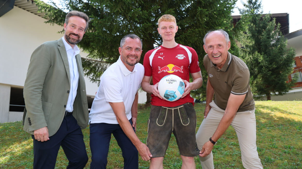 Vier Männer auf einer Wiese beim „1000 Miglia Warm Up Austria 2026“; einer hält einen Fußball in der Hand, alle lächeln.
