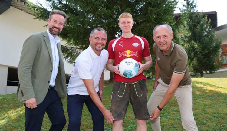 Vier Männer auf einer Wiese beim „1000 Miglia Warm Up Austria 2026“; einer hält einen Fußball in der Hand, alle lächeln.