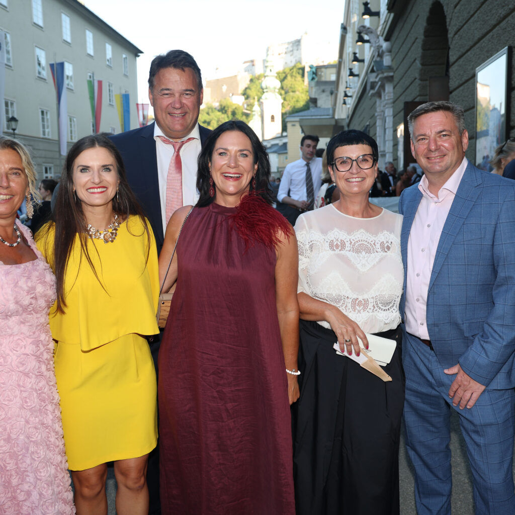 Sechs elegant gekleidete Erwachsene, die bei einer Veranstaltung im Freien lächeln und möglicherweise gemeinsam den UEFA-Superpokal feiern.