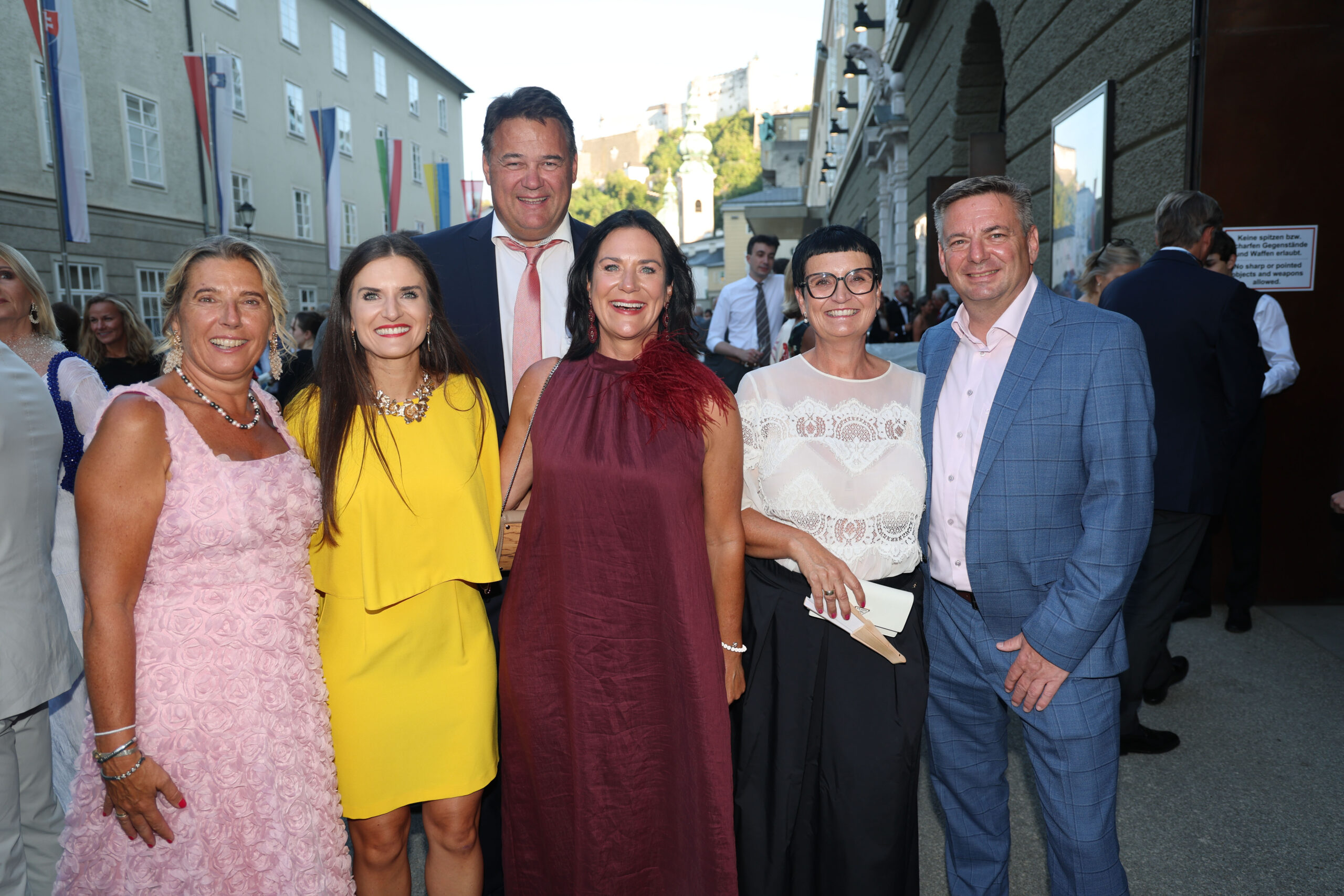 Sechs elegant gekleidete Erwachsene, die bei einer Veranstaltung im Freien lächeln und möglicherweise gemeinsam den UEFA-Superpokal feiern.
