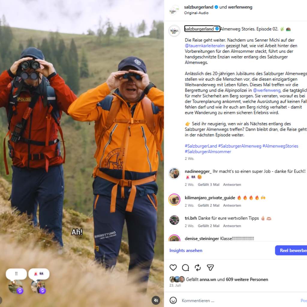Zwei Wanderer in orangefarbenen Jacken genießen die Aussicht auf einem Bergpfad – perfekt für Erinnerungen an den Sommer 2026 in den sozialen Medien.