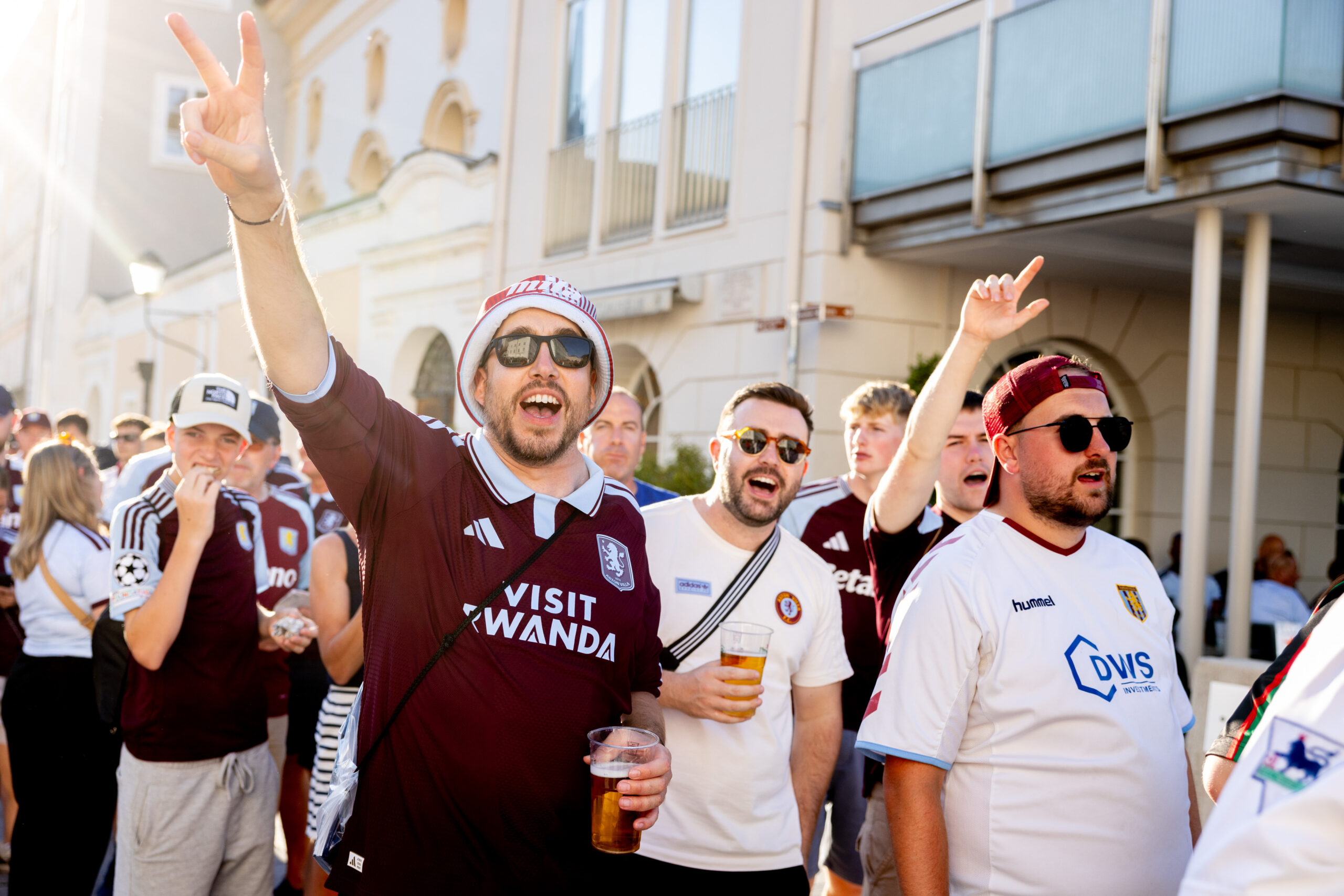 Fans in Fußballtrikots jubeln beim und lächeln draußen im Sonnenschein.