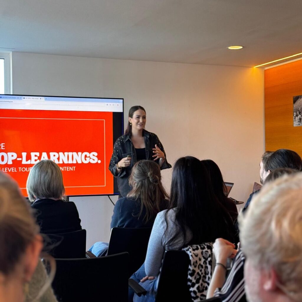Eine Frau hält vor einem sitzenden Publikum einen Vortrag; auf der roten Leinwand hinter ihr steht „LEARNINGS“...